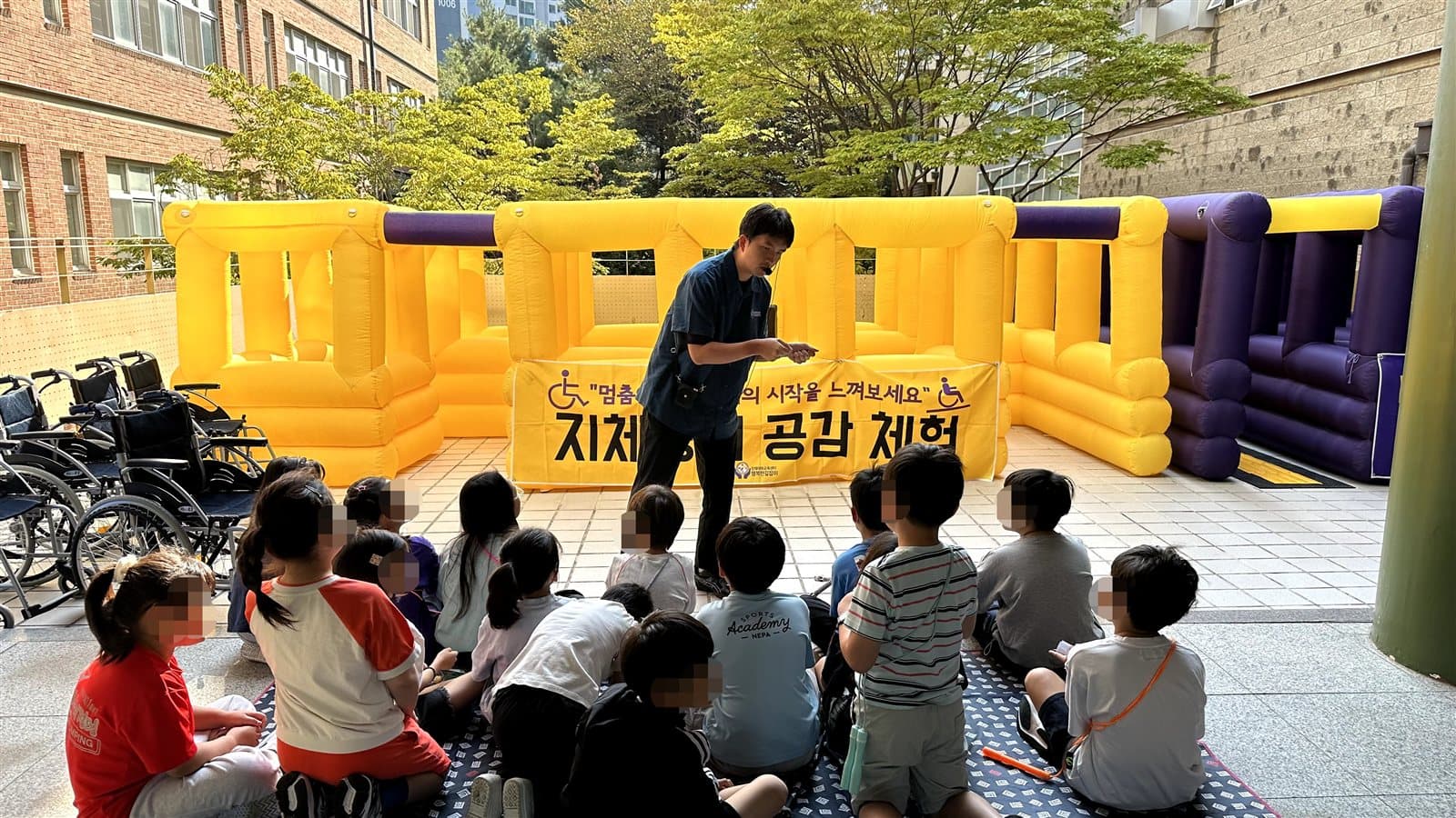 지체장애 공감 체험 배너와 휠체어들 앞에서 강사가 학생들에게 체험 방법을 설명하는 모습